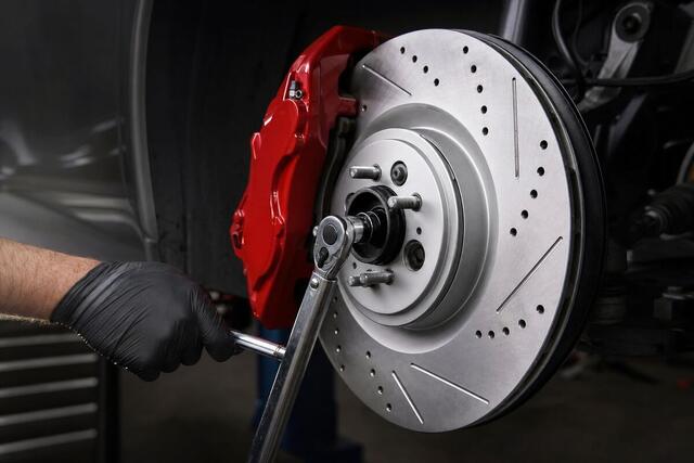 New drilled and slotted brake rotor with a red caliper, mechanic using a torque wrench