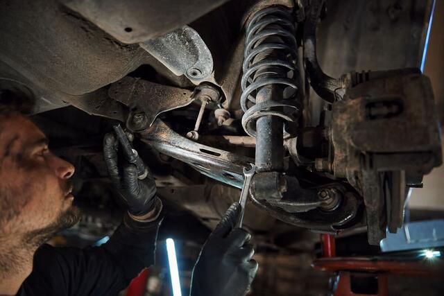 Underside view of a car suspension with coil spring, strut and control arm being serviced