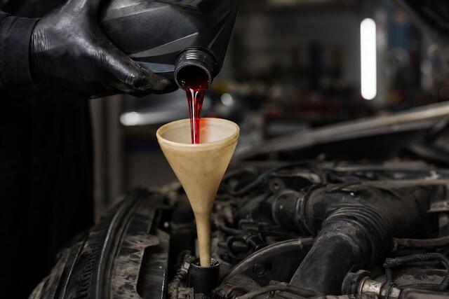 Red automatic transmission fluid being poured through a funnel into a fill tube